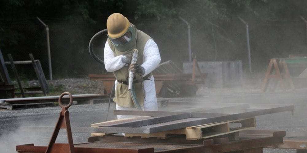 A man in a PPE sand blasting