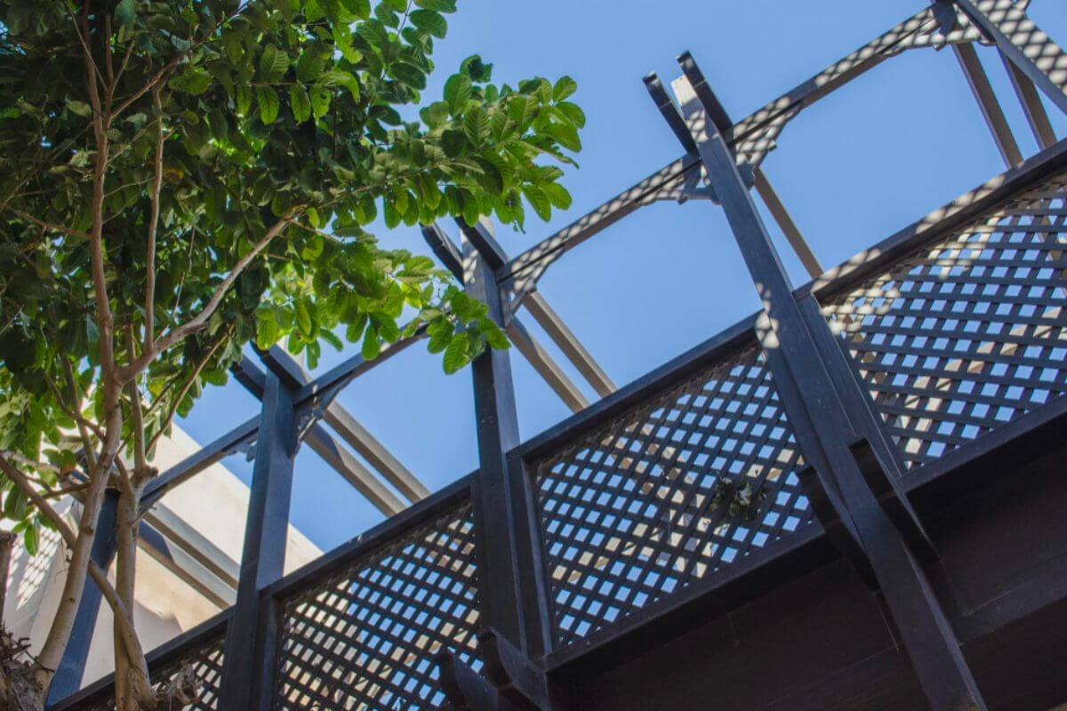 Steel-framed exterior structure with lattice panels and nearby greenery under a clear blue sky