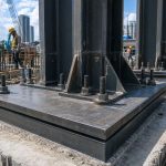 Close-up of steel column base plate with anchor bolts on a reinforced concrete foundation