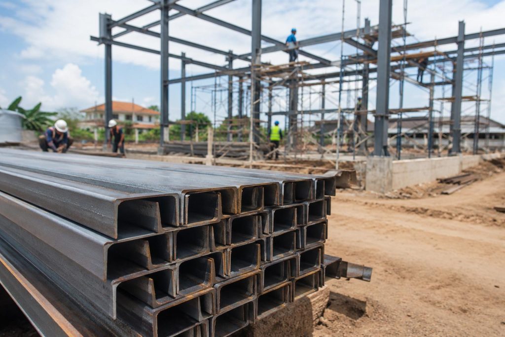 Stacked channel bars at a construction site with steel framing work in the background