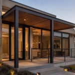 Modern home exterior with exposed black square tube framing, glass walls, and steel canopy design